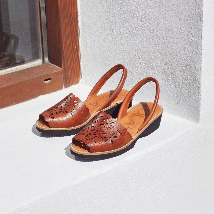 Sandalia menorquina lola Almagro con cuña y grabados florales en la pala de la sandalia color cuero puestas en una ventana