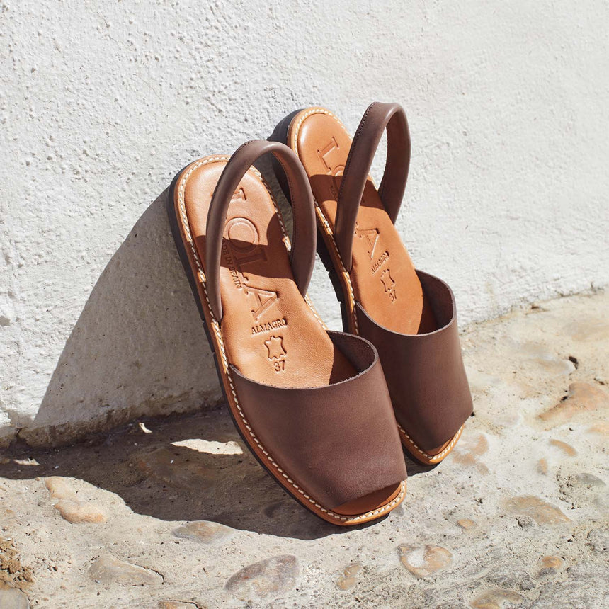 Menorquinas planas de piel de color marrón apoyadas en una pared vista desde el ángulo frontal