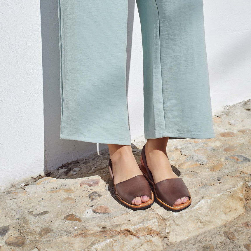 Menorquinas planas de piel de color marrón puestas en los pies de una modelo vista desde el ángulo frontal